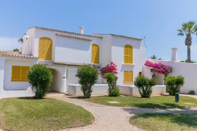 a white house with yellow shutters and pink flowers at AL - Aldeia do Golfe Retreat in Vilamoura