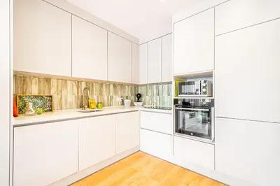 a white kitchen with wooden floors and white cabinets at BeGuest Falésia Beach & Barbecue Apartment in Albufeira