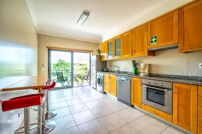 a kitchen with wooden cabinets and a table with red chairs at Monte Balaia AT19 Duplex - Pool View Olhos de Agua in Olhos de Água