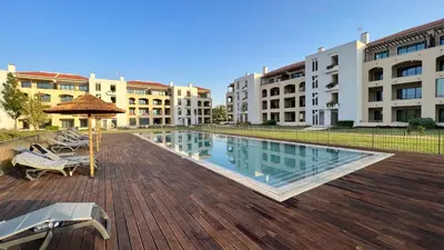 a swimming pool with chairs and an umbrella and some buildings at Apartamento T2 novo e espaçoso em Vilamoura in Vilamoura