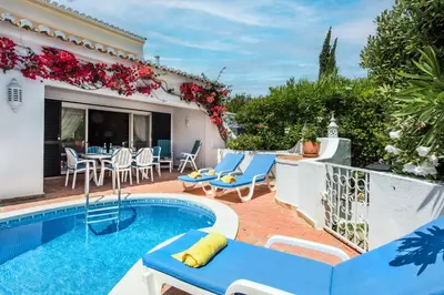 a swimming pool with blue and white chairs next to a house at Mng Elliott76 in Vale do Lobo