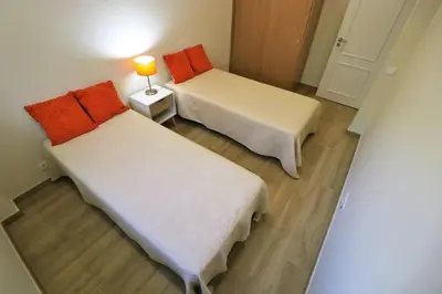 two beds in a room with a lamp on a table at Apartamento laranja Quarteira in Quarteira