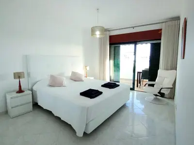 a white bedroom with a white bed and a chair at Beachfront flat with pool in Quarteira