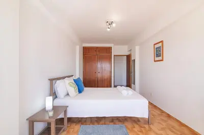a bedroom with a white bed and a wooden floor at Quarteira Mar à Vista T1 in Quarteira