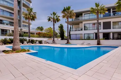a swimming pool in front of a building with palm trees at Стильный апартамент Т2 Quarteira in Quarteira