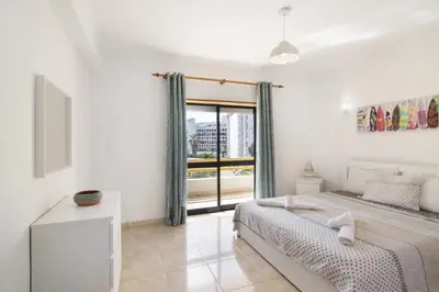 a white bedroom with a bed and a window at Hilcity in Albufeira