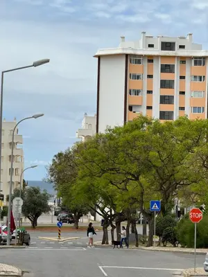 people crossing a street in front of a tall building at Princess Retreat Beautiful Modern Aprt 2 min walk from Quarteira Beach in Quarteira