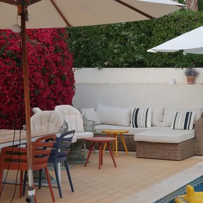 a patio with white couches and tables and red flowers at Santos Villa in Quinta do Lago in Quinta do Lago