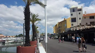people walking down a street next to a marina with palm trees at Vilamoura Dream House QR2 in Quarteira