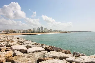 a beach with rocks and a city in the background at Vacation Apartment in Quarteira in Cavacos
