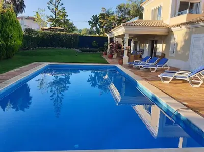 a blue swimming pool in front of a house at Luxury Private 5 bedroom Villa pool, golf, Algarve in Quarteira