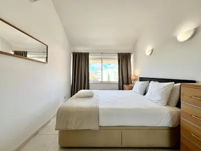 a white bedroom with a large bed and a window at Home Out - Vilamoura Beach Apartment - Duplex in Quarteira