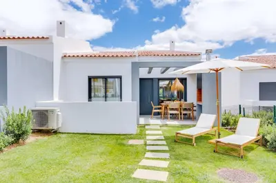a white house with a yard with chairs and an umbrella at AL - Villas Country Club in Vilamoura