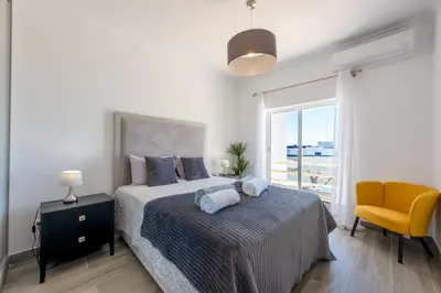 a bedroom with a bed and a chair and a window at Casa Merrigan in Albufeira