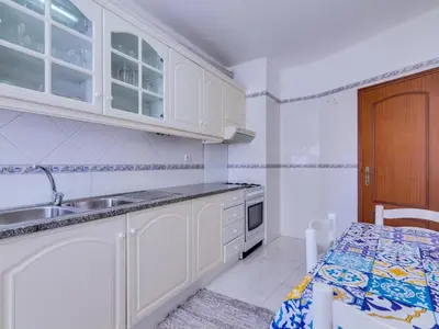 a kitchen with white cabinets and a sink and a table at Central 2bdr apartment in Quarteira in Quarteira
