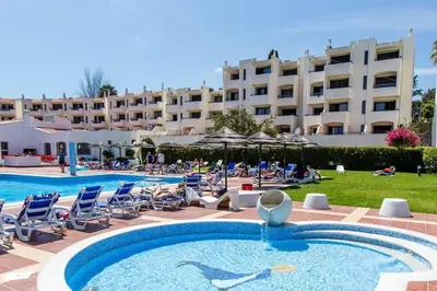 a hotel with a pool and chairs and a building at Apartamento do Moinho acesso à Piscina in Albufeira