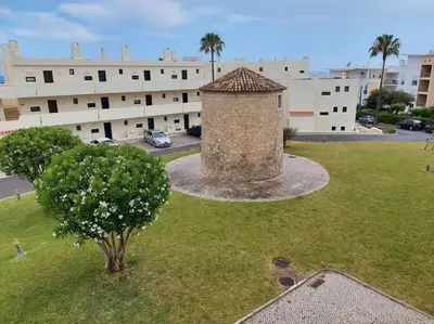 a building with a tower in the grass with a tree at Apartamento do Moinho acesso à Piscina in Albufeira