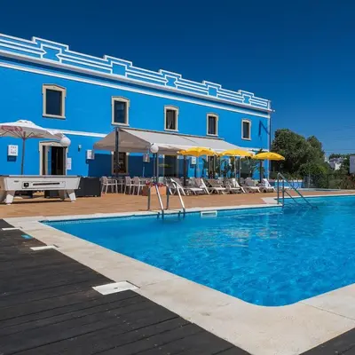 a blue building with a swimming pool with chairs and umbrellas at ADO HOUSE Albufeira in Albufeira