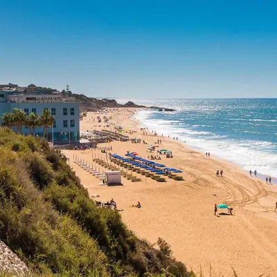 a beach with people and umbrellas and the ocean at ADO HOUSE Albufeira in Albufeira