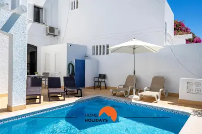 a pool with chairs and an umbrella next to a house at #232 Vila Girasol 33 by Home Holidays in Albufeira