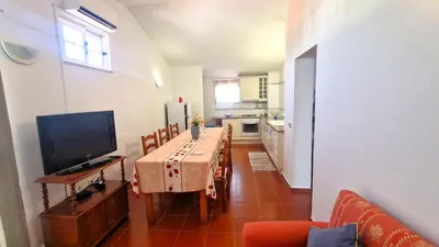 a living room with a table and a television and a kitchen at Apart Alfarrobinha - T2 - BY BEDZY in Tunes
