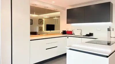 a white kitchen with white cabinets and a television at Refúgio Sereno Vilamoura T2 by HsR Vilamarina in Quarteira