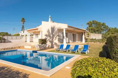 a house with a swimming pool and blue chairs at Villa Costa in Albufeira