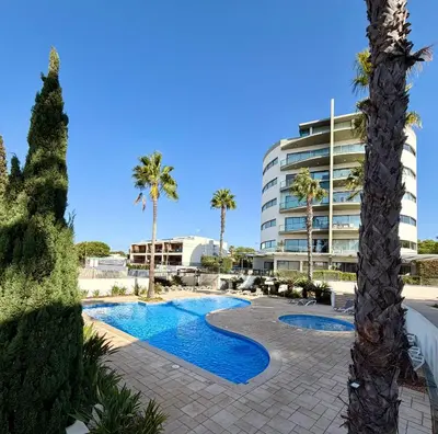 a resort swimming pool with palm trees and a building at Cavalo Preto Beach Resort in Quarteira