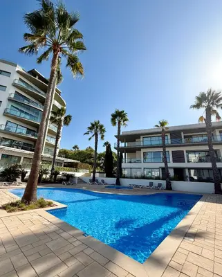 a swimming pool in front of a building with palm trees at Cavalo Preto Beach Resort in Quarteira