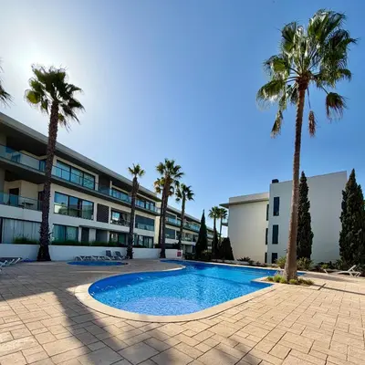 a swimming pool in front of a building with palm trees at Cavalo Preto Beach Resort in Quarteira