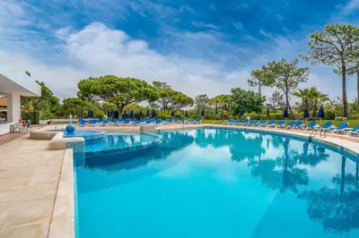 a swimming pool with blue chairs and trees at BmyGuest Collection - Quinta do Lago Luxury Beach Apartment in Almancil