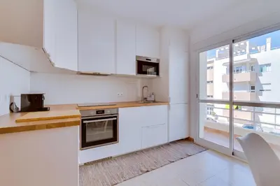a kitchen with white cabinets and a large window at Apartamento Al Sakia 2bdr com piscina e ar condicionado in Quarteira