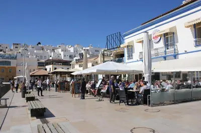 a town square with benches and buildings and a tree at Paulos Studio in Faro