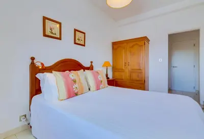 a bedroom with a bed with white sheets and pink pillows at Apartamento Farol com piscina e estacionamento in Vilamoura