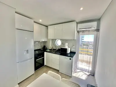 a kitchen with white cabinets and a table and a window at Julio Apartment in Albufeira