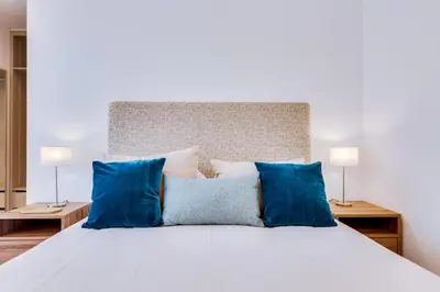 a large white bed with blue pillows on it at Apartamento Gaivota frente-mar in Quarteira