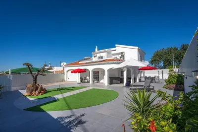 a white house with red umbrellas in a yard at Casa da Amélia in Albufeira