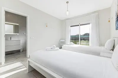 a white bedroom with a large bed and a window at Quinta dos Figos - Jacuzzi Perto da Praia in Guia