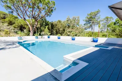 a swimming pool with a wooden deck next to a tree at Casa da Alegria, Vale do Lobo in Almancil