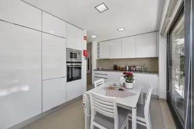 a white kitchen with a table and white cabinets at Areias Branca in Quarteira