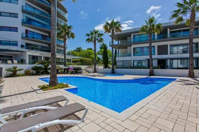 a swimming pool in front of a building with palm trees at Sol e Mar in Quarteira