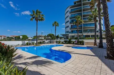 a swimming pool with palm trees and a building at Sol e Mar in Quarteira