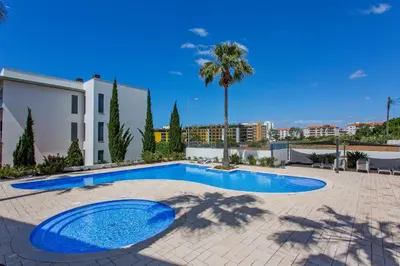 a swimming pool in a courtyard with a building and palm trees at Vista Mar in Quarteira