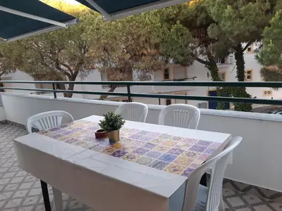 a white table and chairs on a balcony with a table and a plant at Beach Falésia in Albufeira