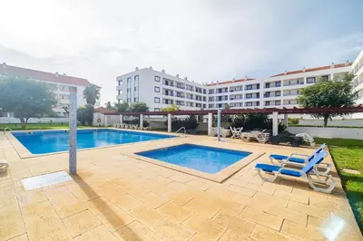 a swimming pool with two blue chairs and a building at Vilamoura Family Escape in Quarteira