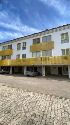 a building with yellow balconies and cars parked in front at Apartamento a 5 min a pé da praia, com terraço grande ao sol, no Rés-Chão in Quarteira