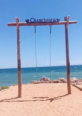 a sign on the beach with two swings at Apartamento a 5 min a pé da praia, com terraço grande ao sol, no Rés-Chão in Quarteira