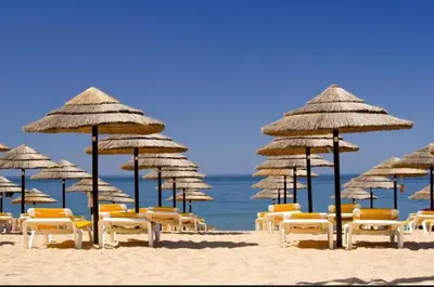 a group of chairs and umbrellas on a beach at Apartamento a 5 min a pé da praia, com terraço grande ao sol, no Rés-Chão in Quarteira