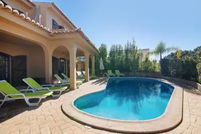 a swimming pool in a yard with chairs and a house at Villa Rústica in Albufeira