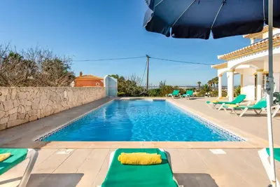 a pool with chairs and an umbrella next to a house at Villa Agapito in Terras Novas